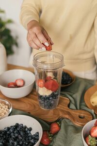 Frau bereitet einen Smoothie aus verschiedenen Beeren in einem Mixer zu