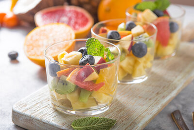 Obstsalat in Gläsern mit Orangen, Kiwi, Blaubeeren, Ananas und Kokosnuss