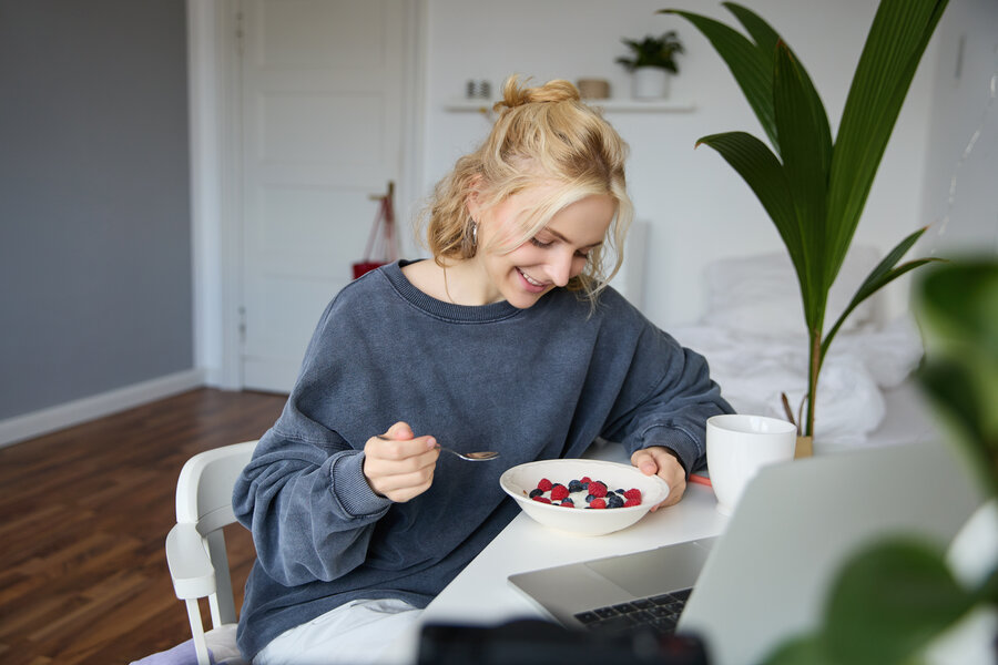 Frau isst Joghurt mit Früchten am Schreibtisch